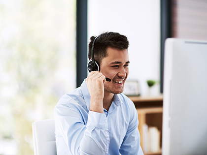 A person in business clothes smiling and wearing a headset, while sitting in front of a computer monitor. 