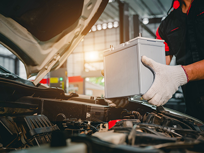 A tradesperson holding a battery over an open car bonnet.