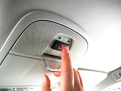 A hand reaching for the SOS button on the ceiling of their car.