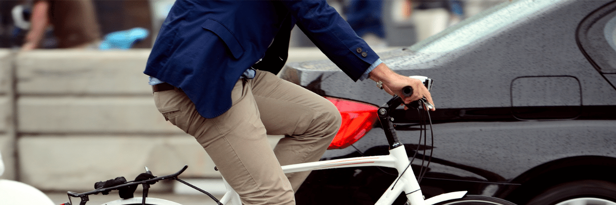 Person in beige pants and blue jacket riding a white bicycle on a wet city street.