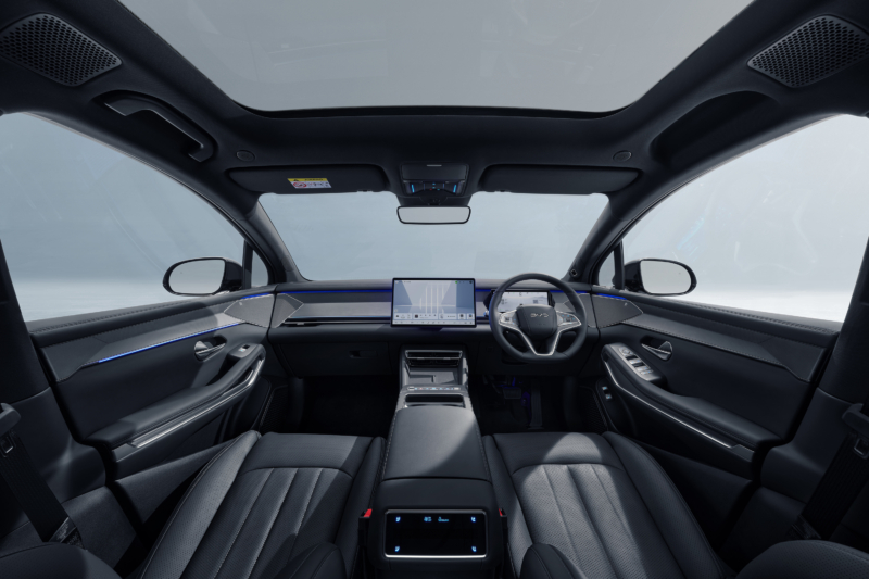 Interior of the BYD Sealion 8 viewed from the rear seats, showing the panoramic glass roof, large central touchscreen, right-hand-drive steering wheel and tech-focused interior featuring eCall button, service provided by Intelematics.